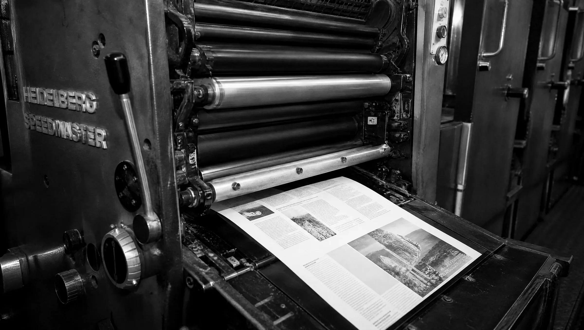 Druckwerk einer Heidelberger Offsetmaschine mit Farbwalzen und laufendem Druckbogen, schwarz-weiß